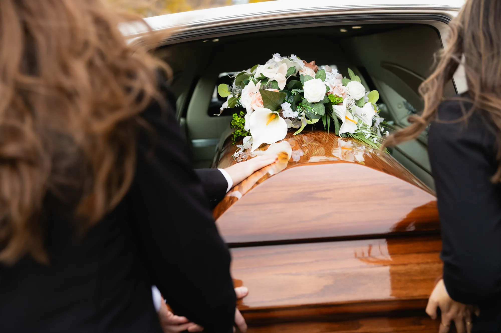 Two Generations funeral directors setting a floral spray on a casket at the hearse