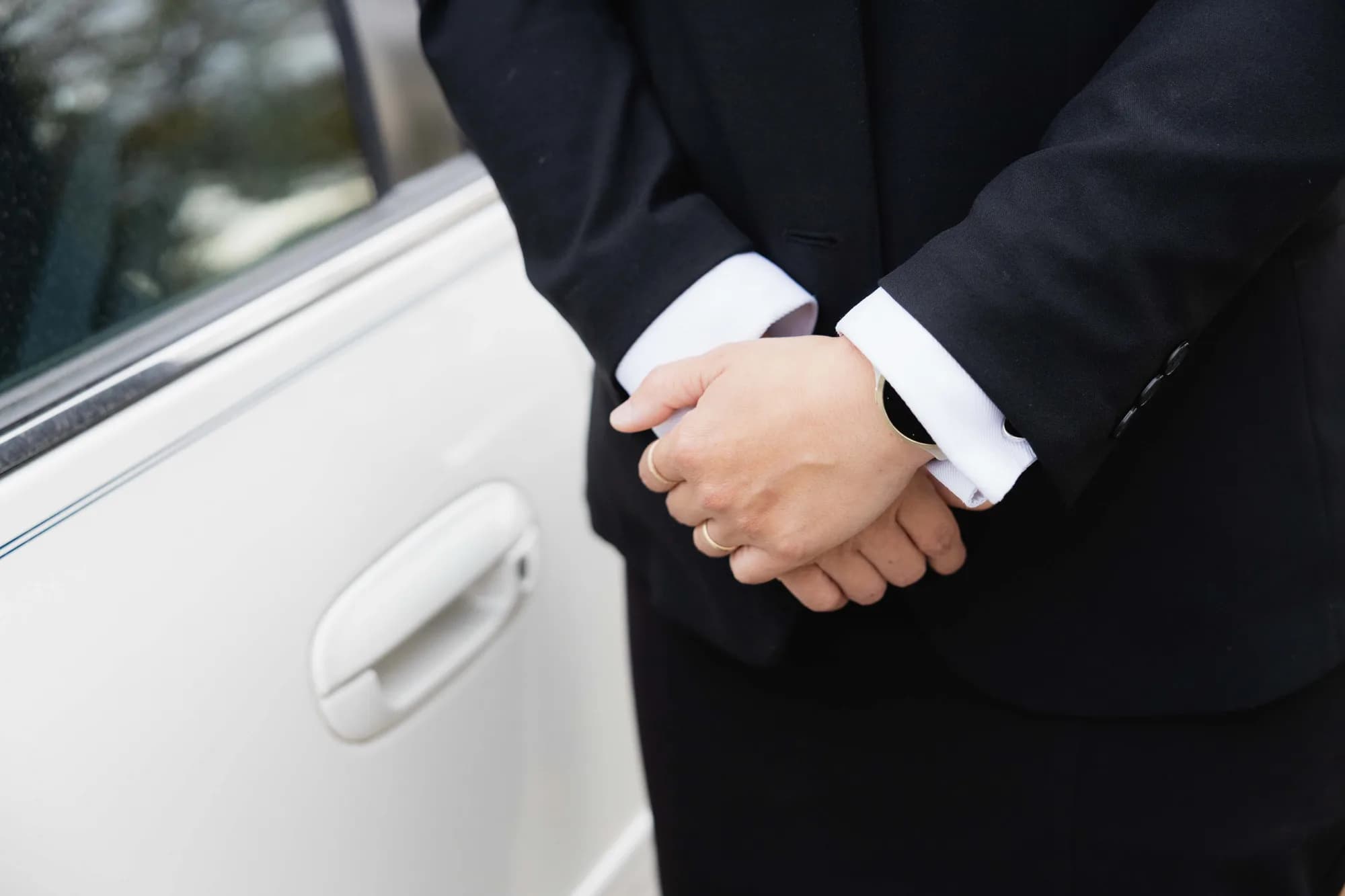 A Generations funeral director standing with hands folded beside the car